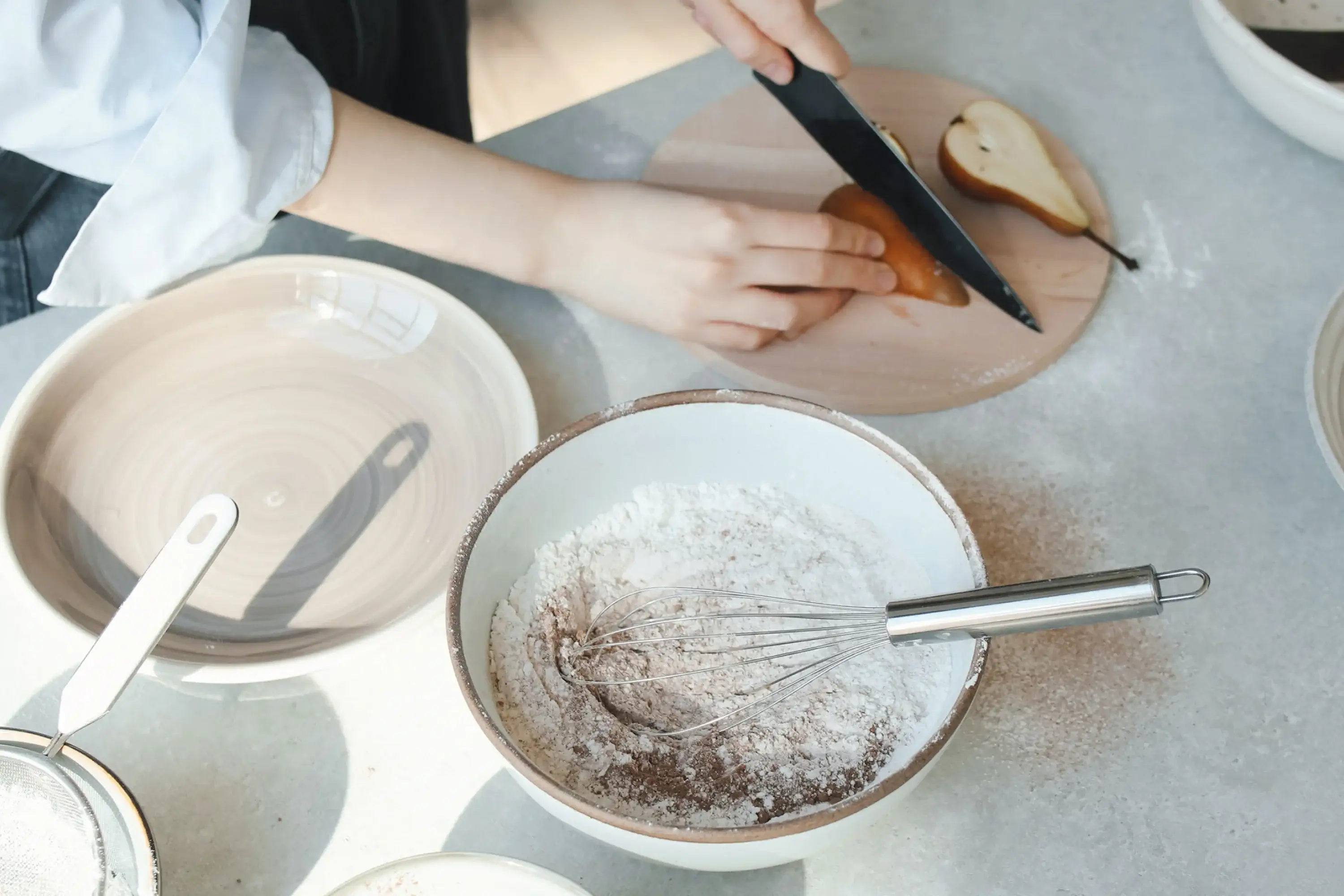 person cutting a pear with bowls of flour next to them